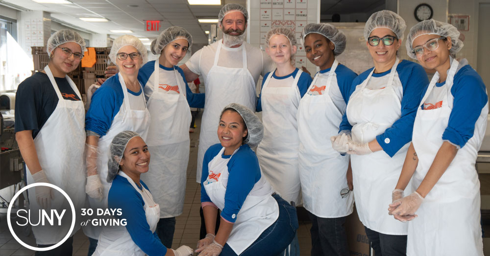 Students and staff from the Fashion Institute of Technology pose for a picture with actor Hugh Jackman with everyone wearing food nets and aprons in a commercial kitchen.