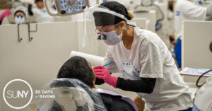 Student dentist check on the mouth of a patient in a dental chair.