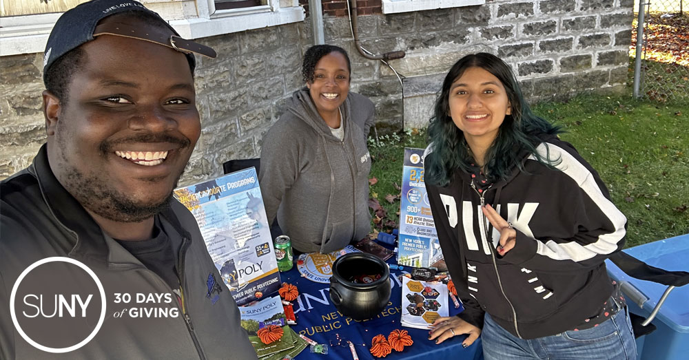 SUNY Polytechnic Institute EOP students pose for a picture at their table outdoors during a community trick or treat event.