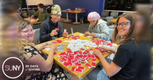 Students at Tompkins Cortland Community College sit at a table in the student lounge with many red stickers in a pile on it.