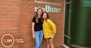 Two female students stand outside a campus building entryway at Ulster County Community College.