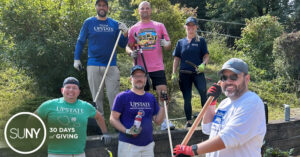 Staff from Upstate Medical University pose with their rools after raking and sweeping an outdoor play space.
