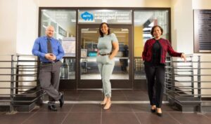 Patrick Rosenberger Dixie Farr, and Jacqueline Hall stand in a row outside of a set of glass doors. A sign on the door reads, "Buffalo Employment and Training Center"