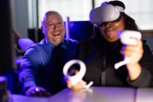 Patrick Rosenberger sits in the background while working with a woman wearing a virtual reality headset participates in a VR simulation.