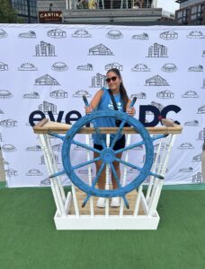  Annalisa Alicea stands in front of a back drop and poses with a blue ship's wheel