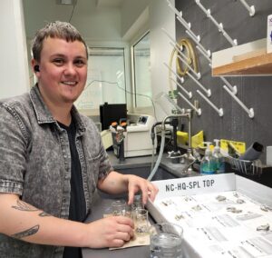 Collyn Dungey stands in a lab setting with samples to his right.