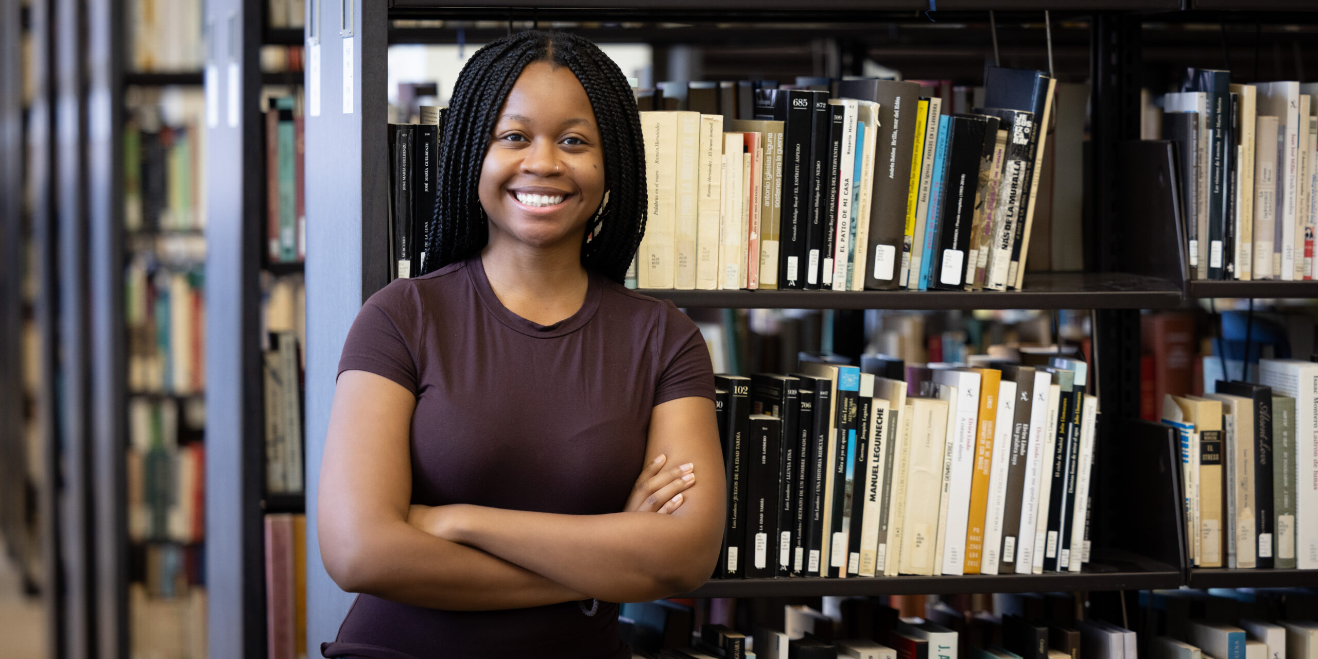 Trinity, UAlbany student, in library in front of books