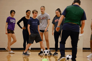 SUNY Cortland students work with children as part of the Special Olympics, as one child dribbles a soccer ball