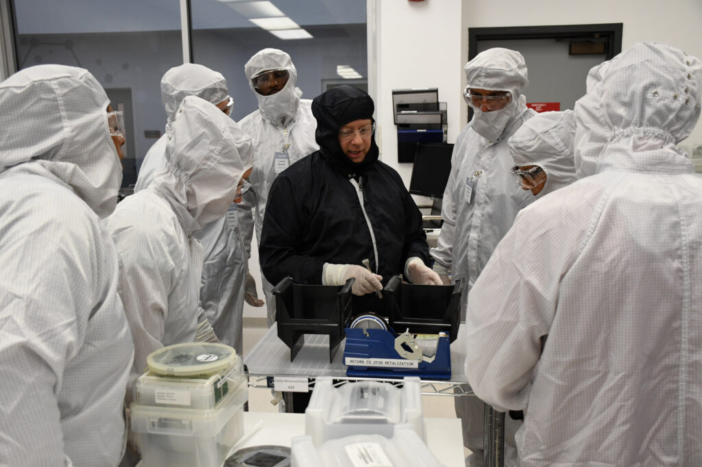 Students and researchers in cleanroom suits participate in hands-on semiconductor manufacturing training in a laboratory environment.